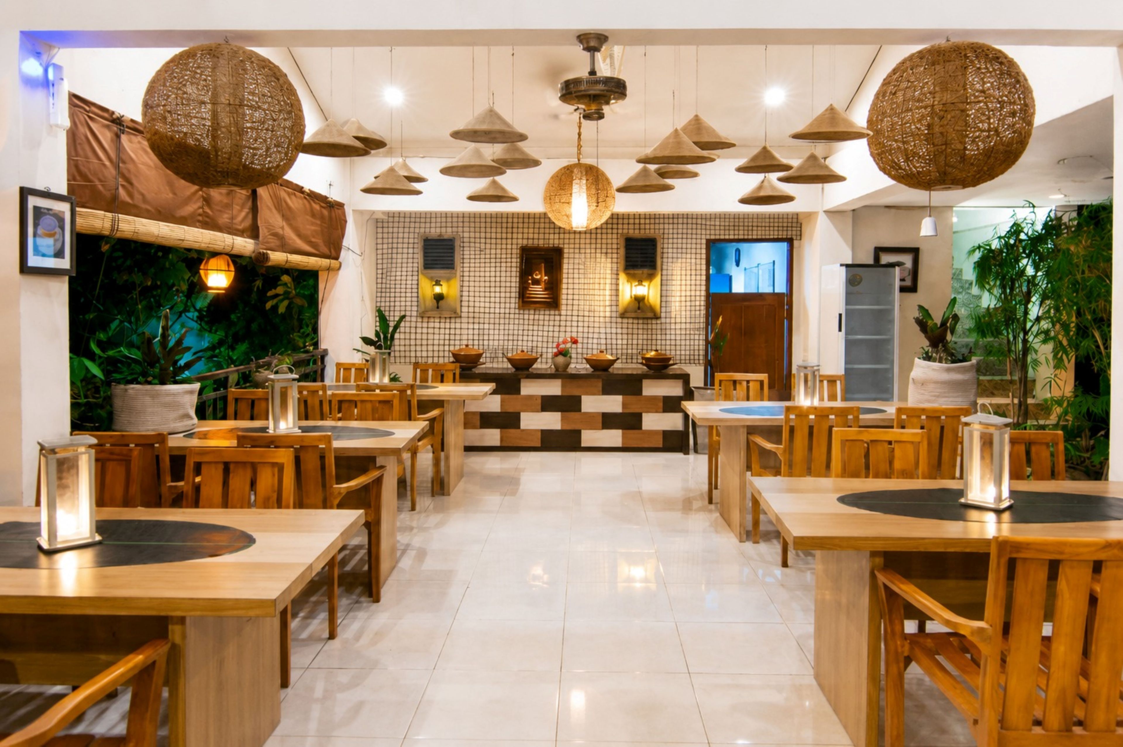 Interior de restaurante com mesas e cadeiras de madeira, luminárias cônicas pendentes e padrão de parede quadriculado.