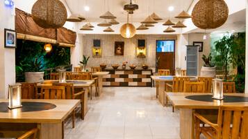 Interior de restaurante com mesas e cadeiras de madeira, luminárias cônicas pendentes e padrão de parede quadriculado.
