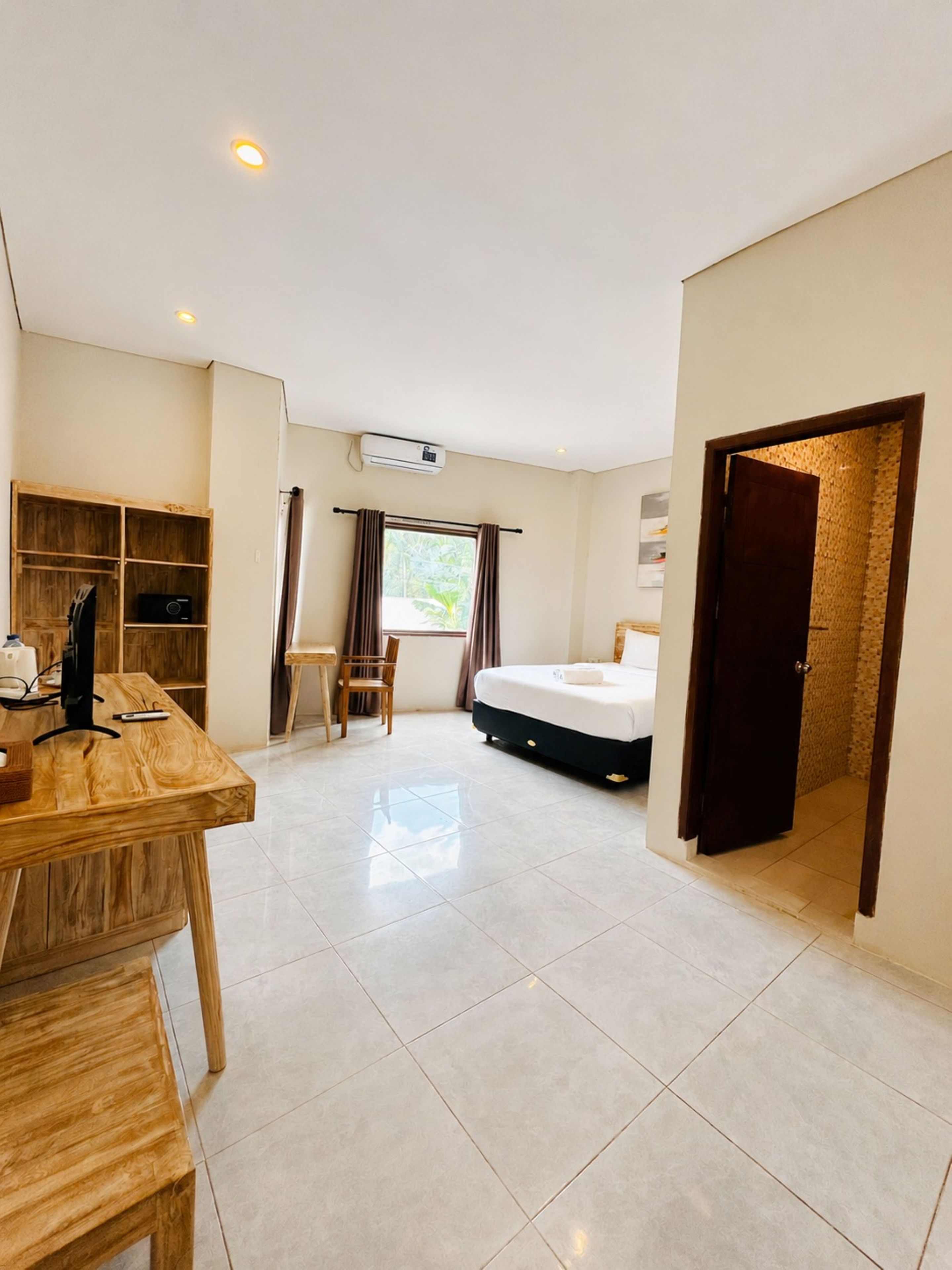 A hotel room with a bed, a desk, a chair, a wardrobe, and a window with curtains.