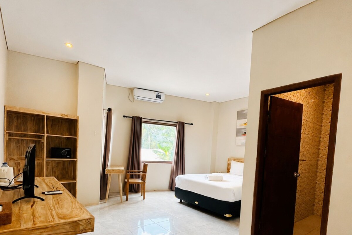 Quarto de hotel com cama, escrivaninha com computador, cadeira e guarda-roupa.