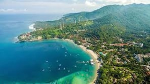 Vista aérea de uma área costeira com praia, barcos e vegetação exuberante.