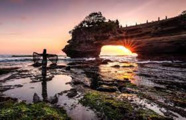 Paisagem costeira com formação rochosa e pôr do sol.