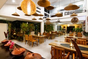 A restaurant with multiple dining tables and chairs, hanging pendant lights, and indoor plants. - Diva Lombok Resort (Senggigi)