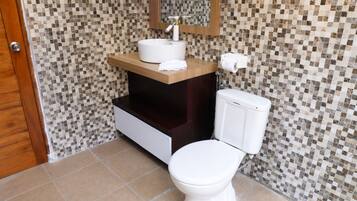 A bathroom with a tiled mosaic wall, a white toilet, a sink with a mirror above it, and a towel on the counter.
