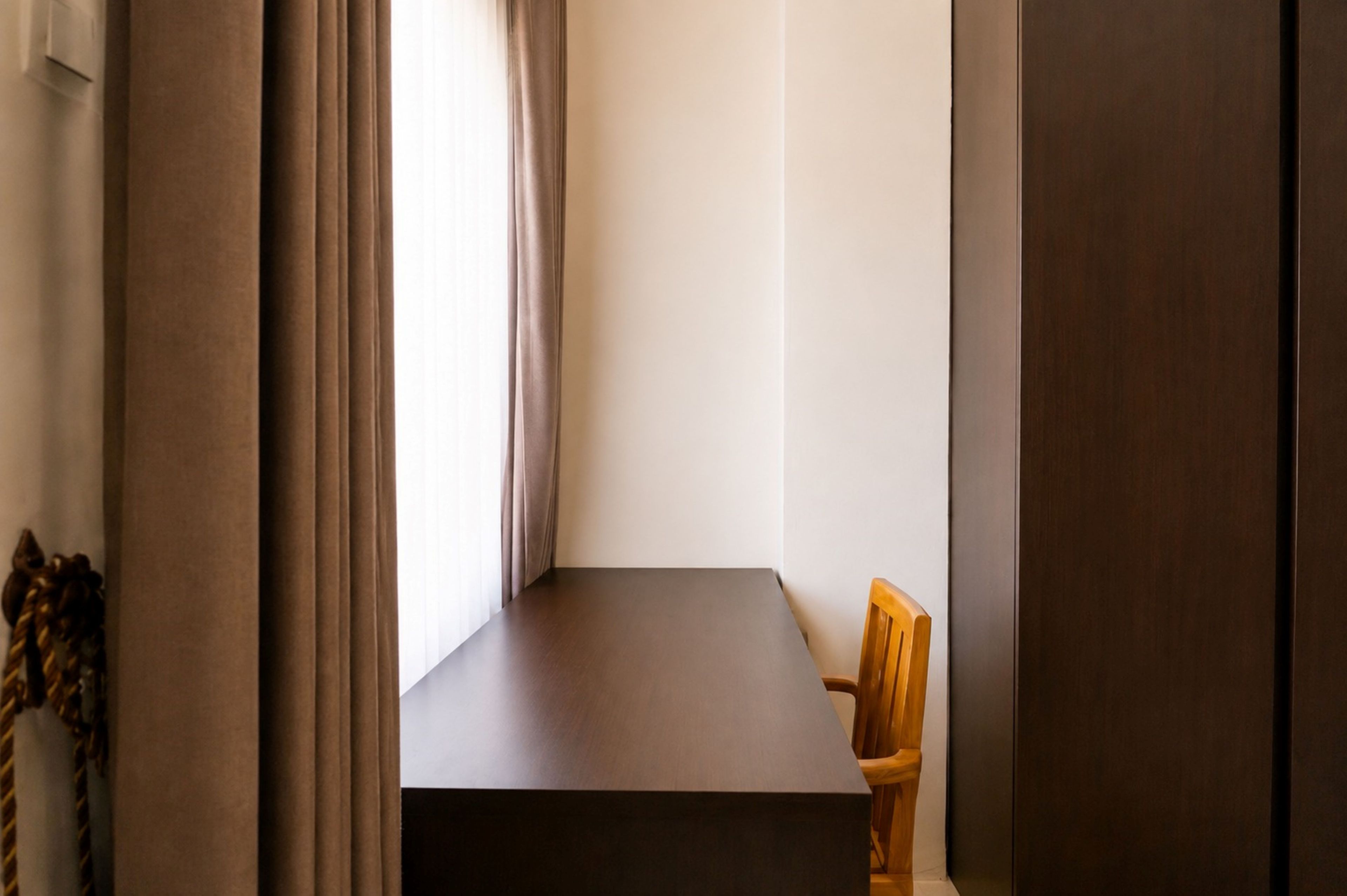 Une pièce étroite, avec une seule chaise en bois, une petite table et une fenêtre avec des rideaux.