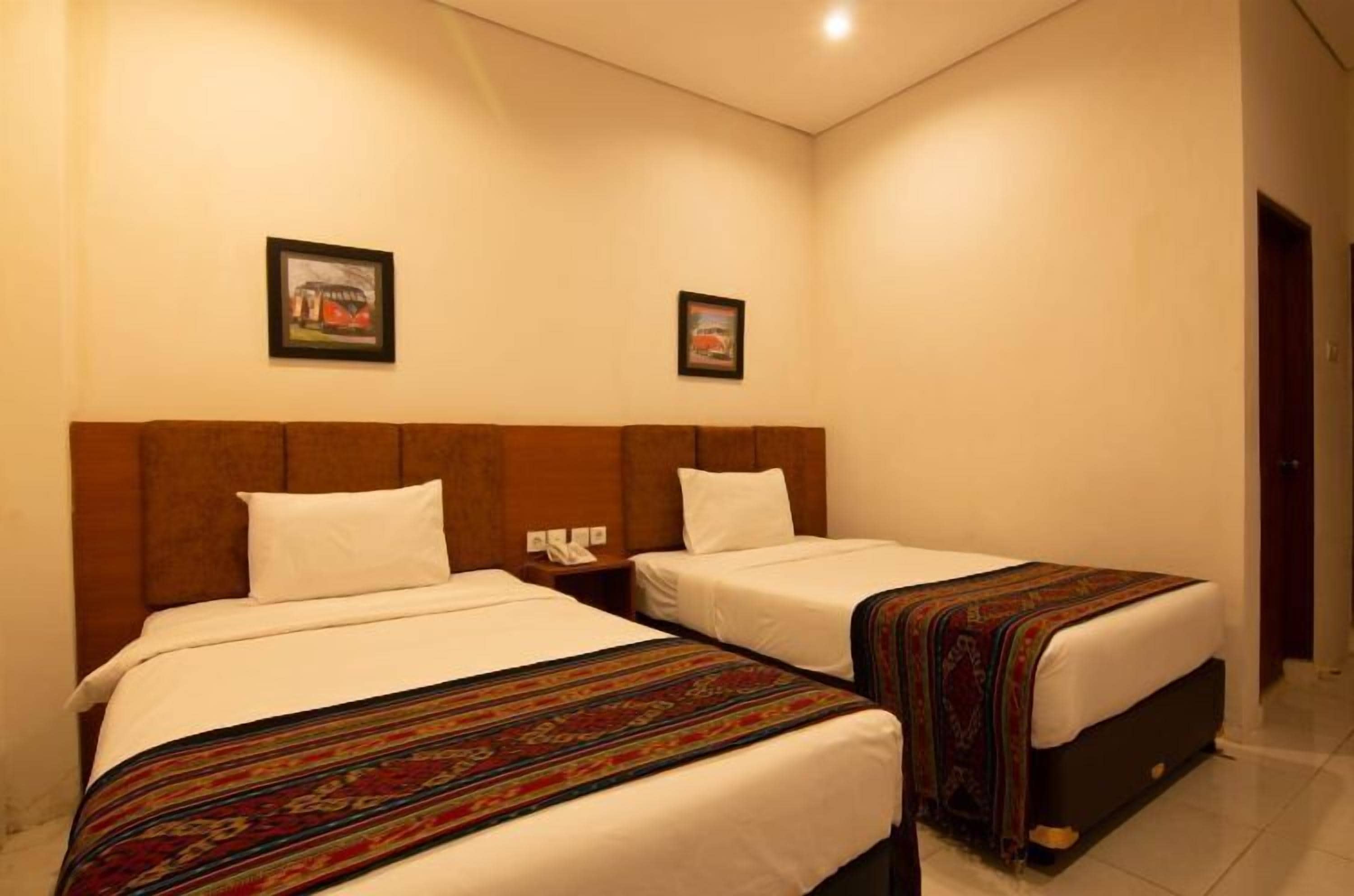 A hotel room with two single beds, a wooden headboard, and a small bedside table with a phone.