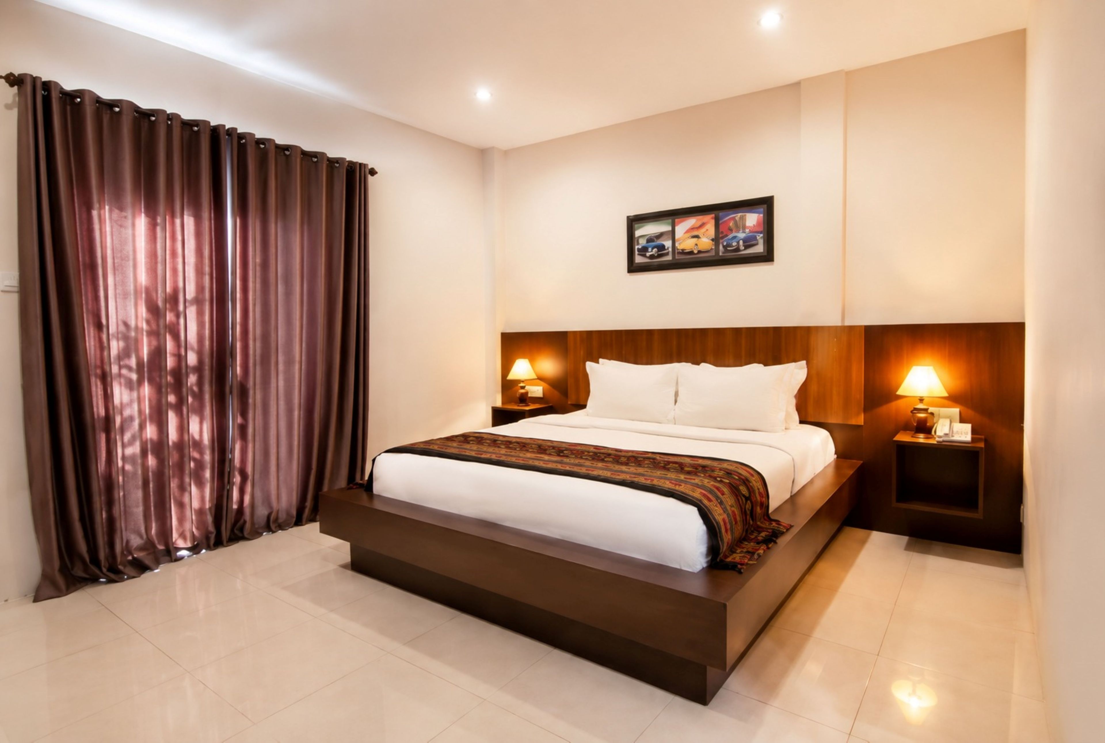 A hotel room with a large bed, two bedside tables with lamps, a wall-mounted picture, and a curtain.