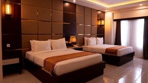 A hotel room with two beds, a large padded headboard, bedside lamps, and a large window with curtains. - Diva Lombok Resort (Senggigi)