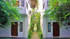 A narrow pathway flanked by lush greenery and wooden doors, leading to a building with a traditional architectural style. - Diva Lombok Resort (Senggigi)