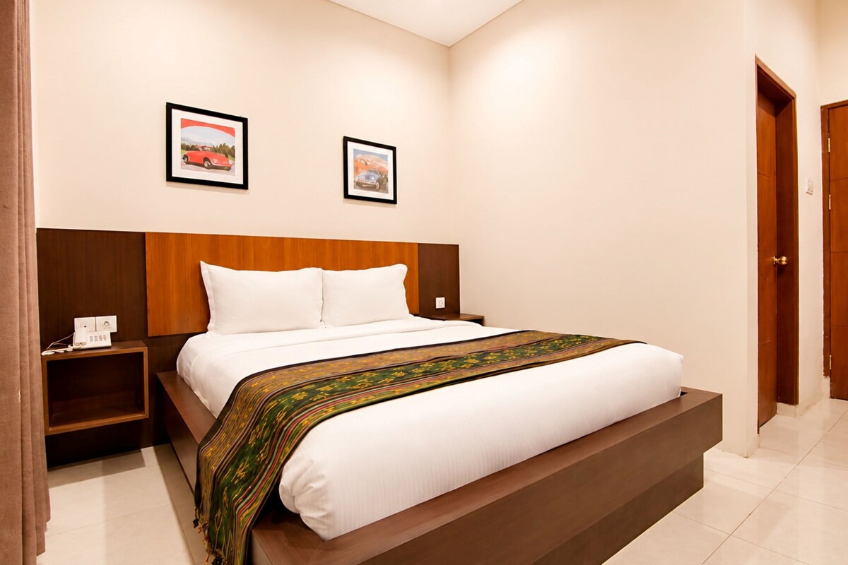 Quarto de hotel com uma cama grande, cabeceira de madeira, duas mesas de cabeceira e duas imagens emolduradas na parede.