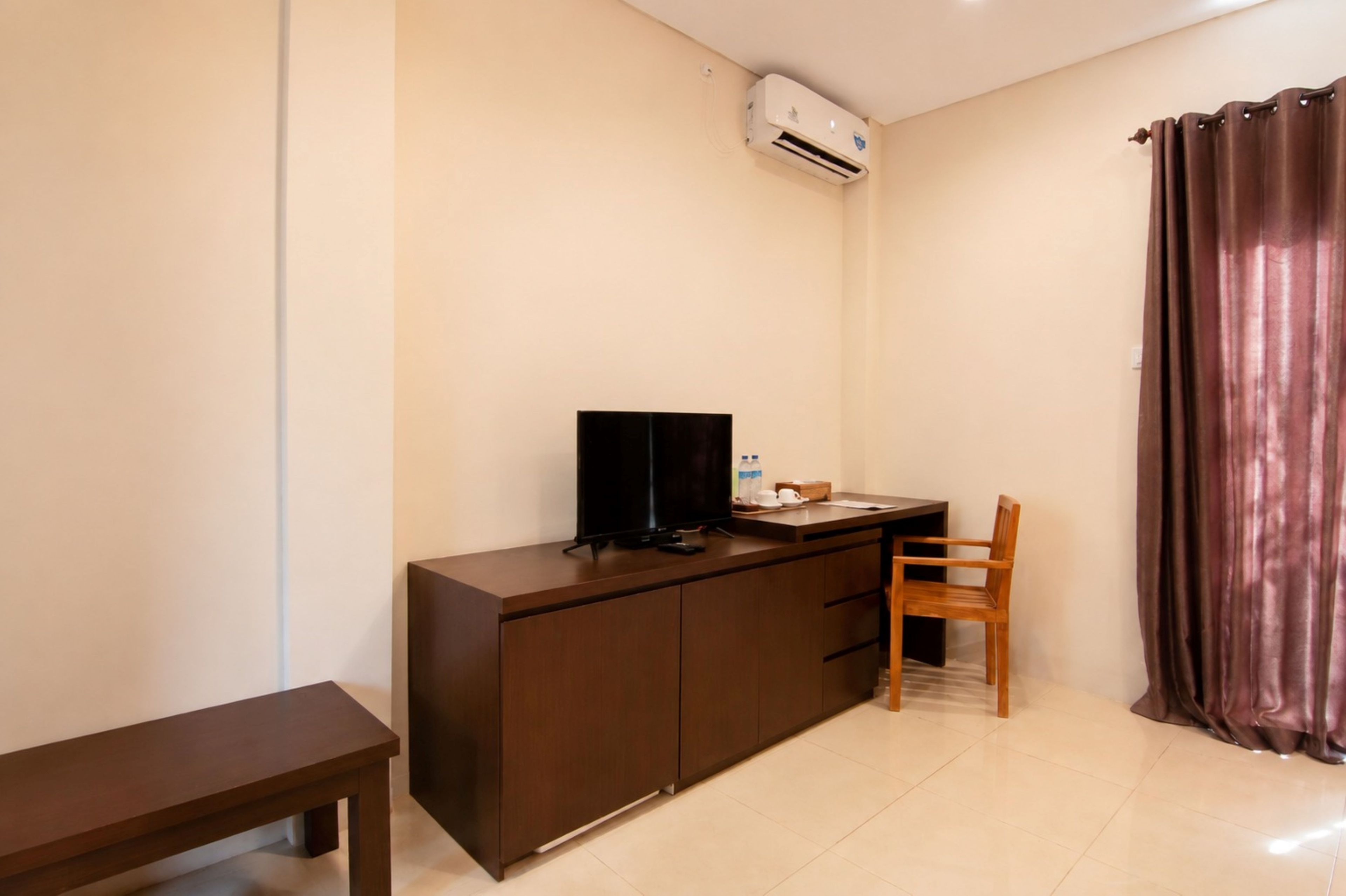 A small, neatly arranged room with a dark wooden desk, a television, a chair, and a brown curtain.