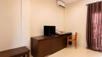 A small, neatly arranged room with a dark wooden desk, a television, a chair, and a brown curtain.