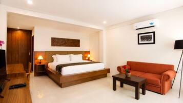 A hotel room with a bed, a sofa, a small table, a TV, and an air conditioning unit.