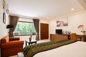A hotel room with a bed, a desk, a television, a chair, and a window with curtains. - Diva Lombok Resort (Senggigi)