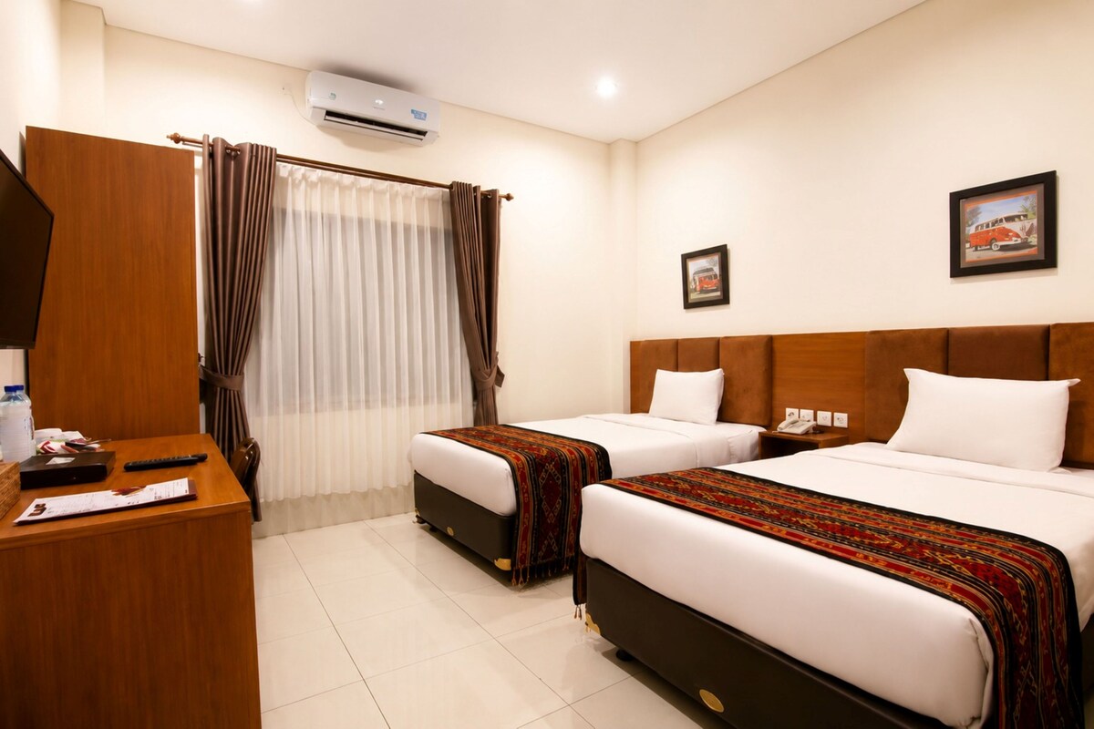 Quarto de hotel com duas camas, uma escrivaninha, ar condicionado e um quadro na parede.