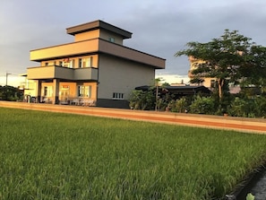 Un edificio moderno de dos pisos con techo plano y fachada lisa, rodeado de un césped cuidado y un sendero pavimentado.