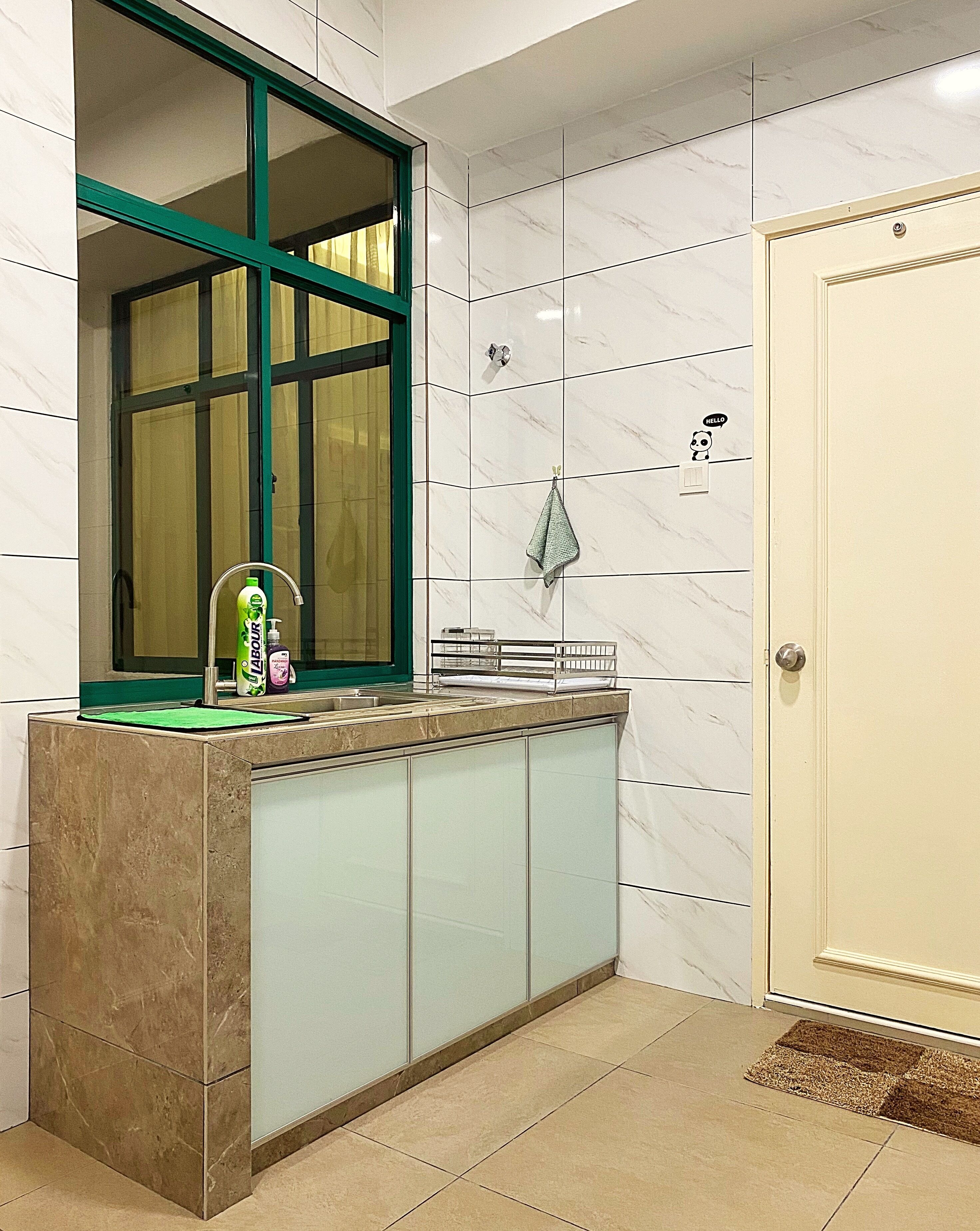 Een badkamer met een marmeren wand, een raam met groene omlijsting, een wastafel met toiletartikelen en een deur met een deurmat.