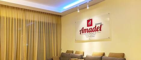 A living room with a sofa set, a glass coffee table, and a sign for Amadel Residence.