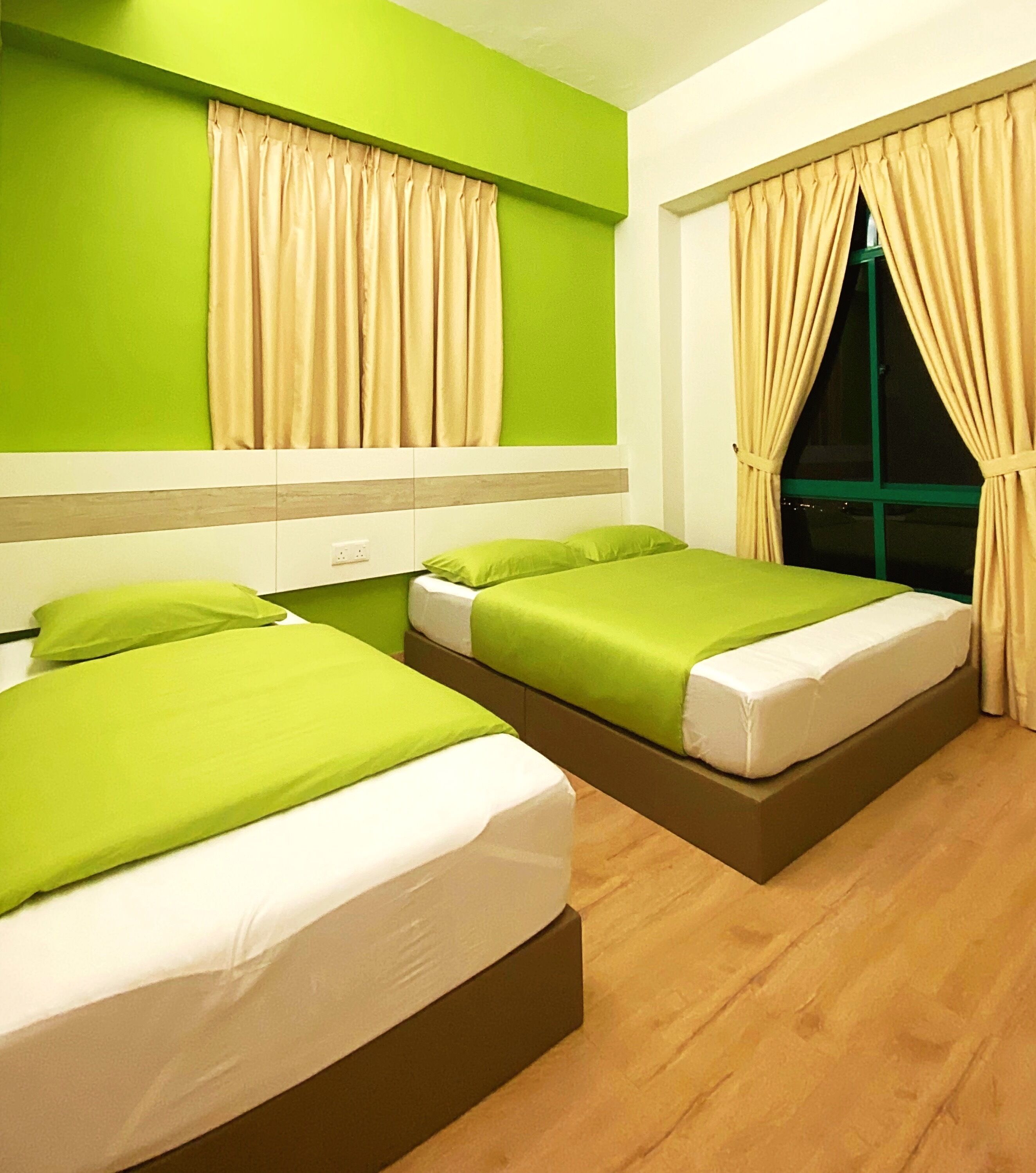 A hotel room with two beds, green bedding, beige curtains, and a green wall.