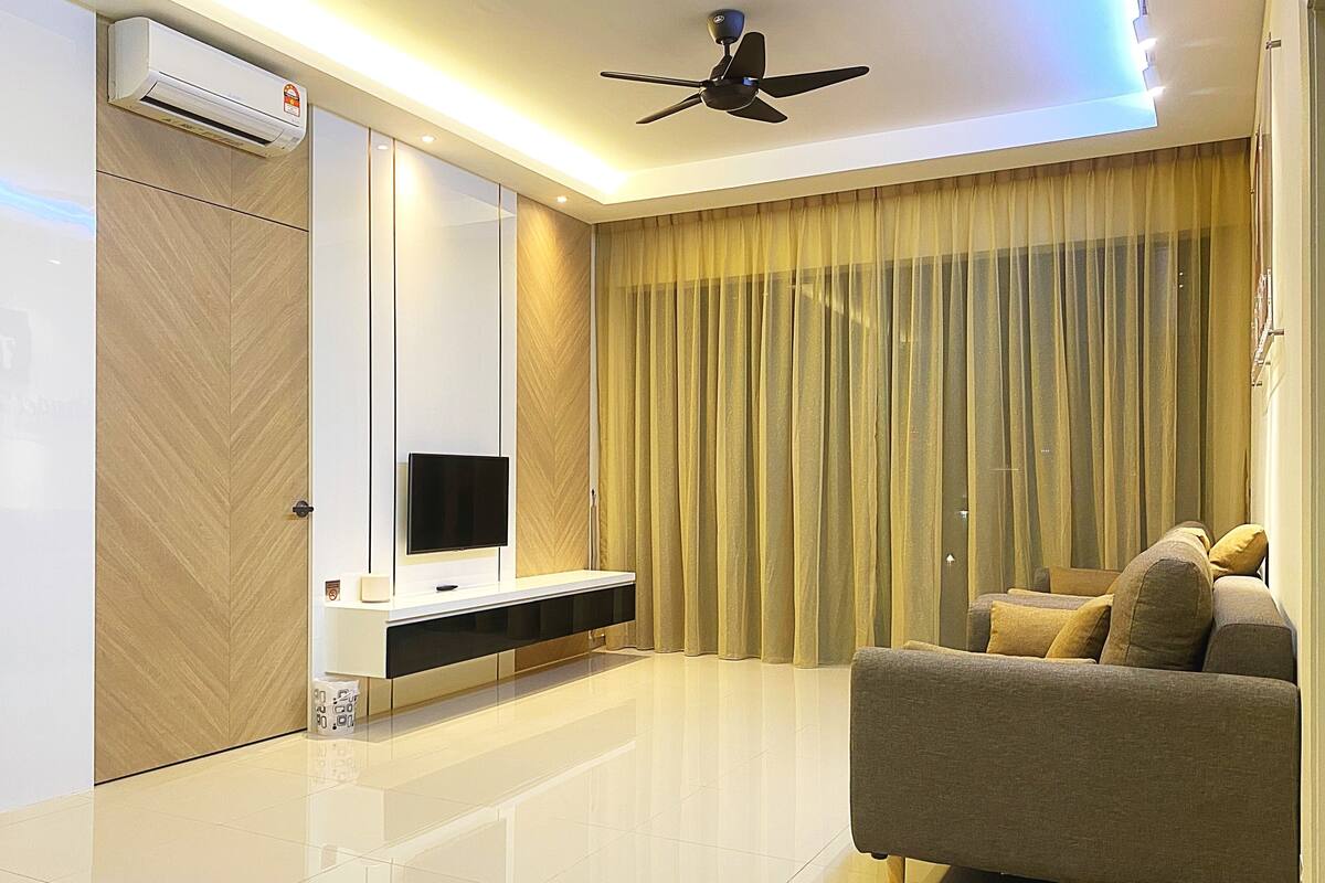 A modern living room with a flat-screen TV, a ceiling fan, and a large window with curtains.