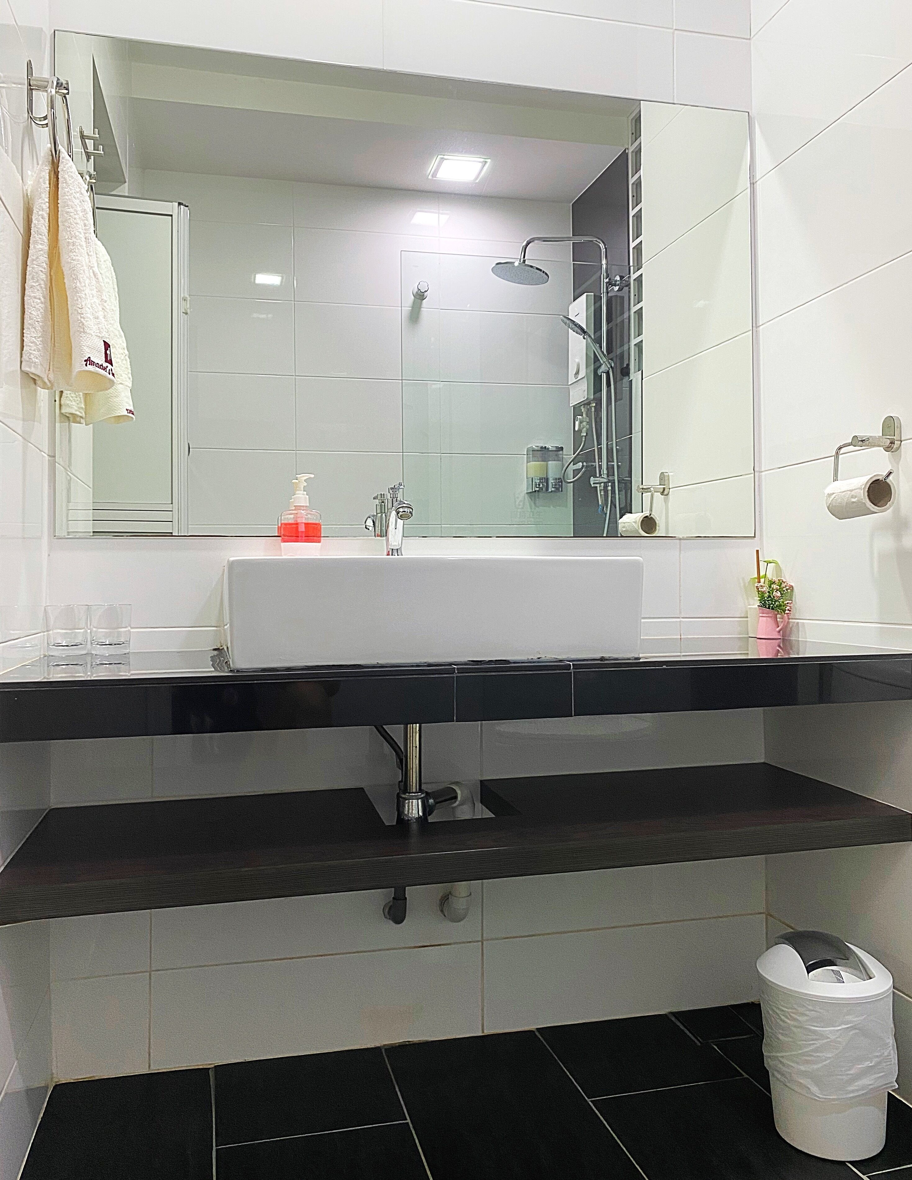 Une salle de bain moderne avec un grand miroir, des carreaux blancs, un plan de travail noir et un lavabo blanc.