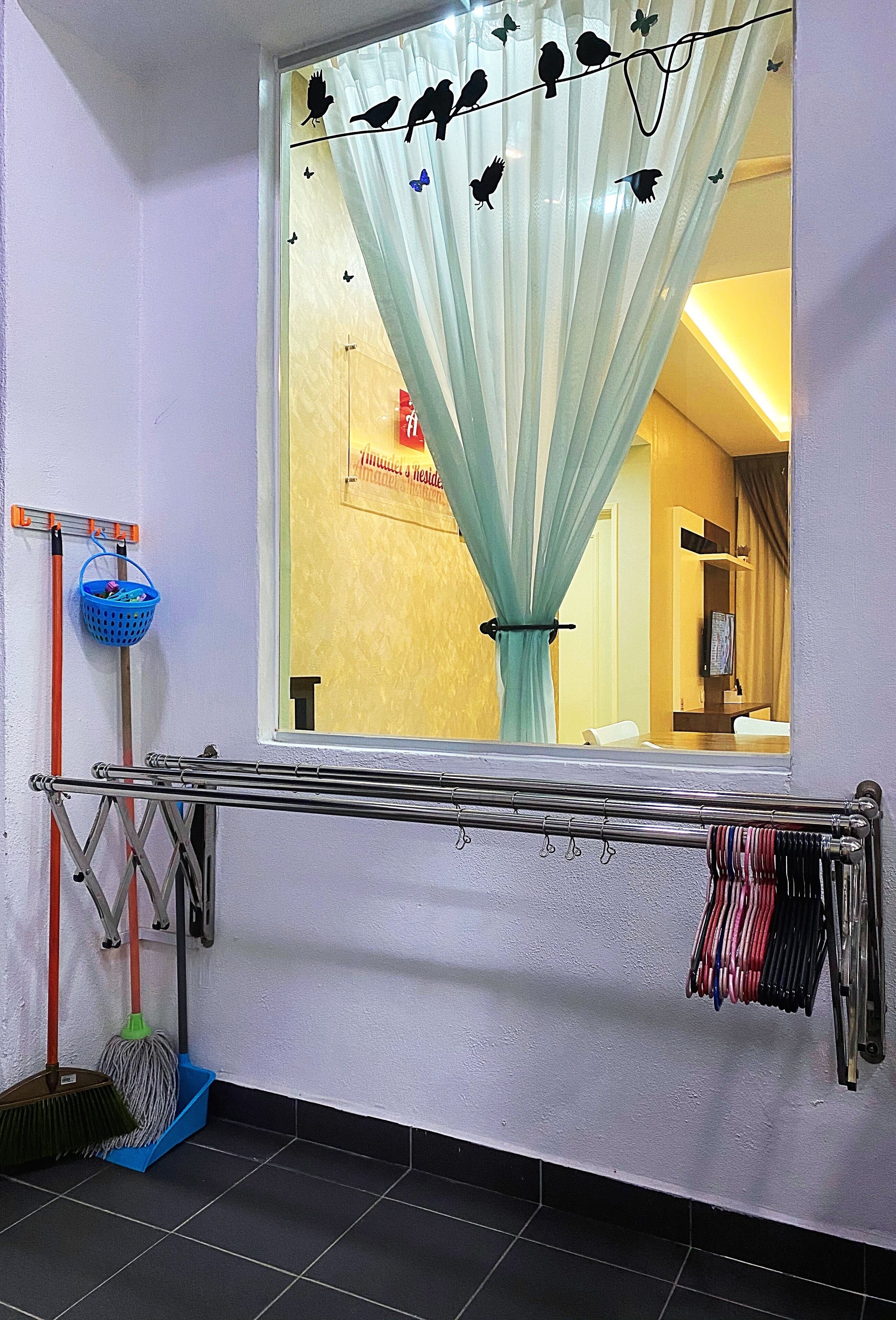 Quarto com janela, varal, esfregão, vassoura e cesto de roupa.