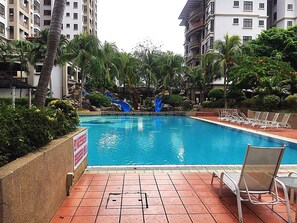 A swimming pool with two blue slides, surrounded by palm trees and lounge chairs.