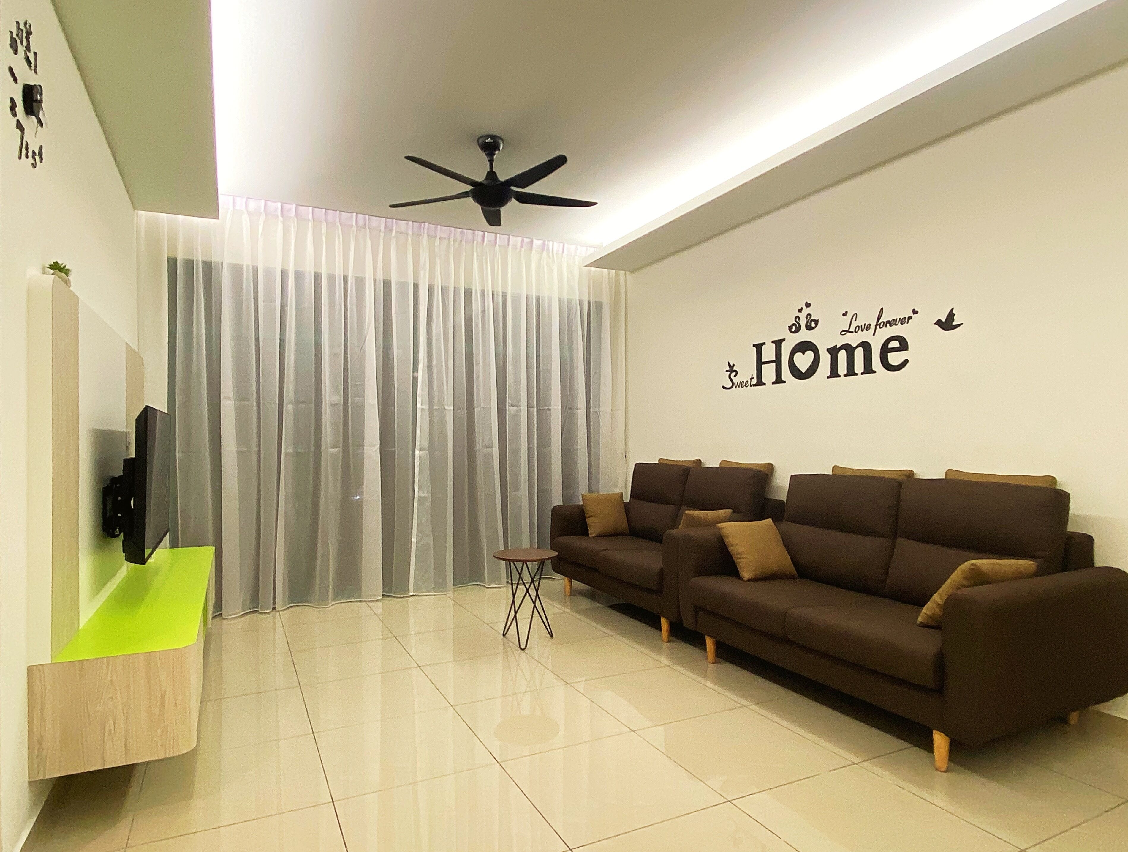 A modern living room with a sofa set, a small side table, a ceiling fan, and a wall with a 'Love Forever Home' sign.