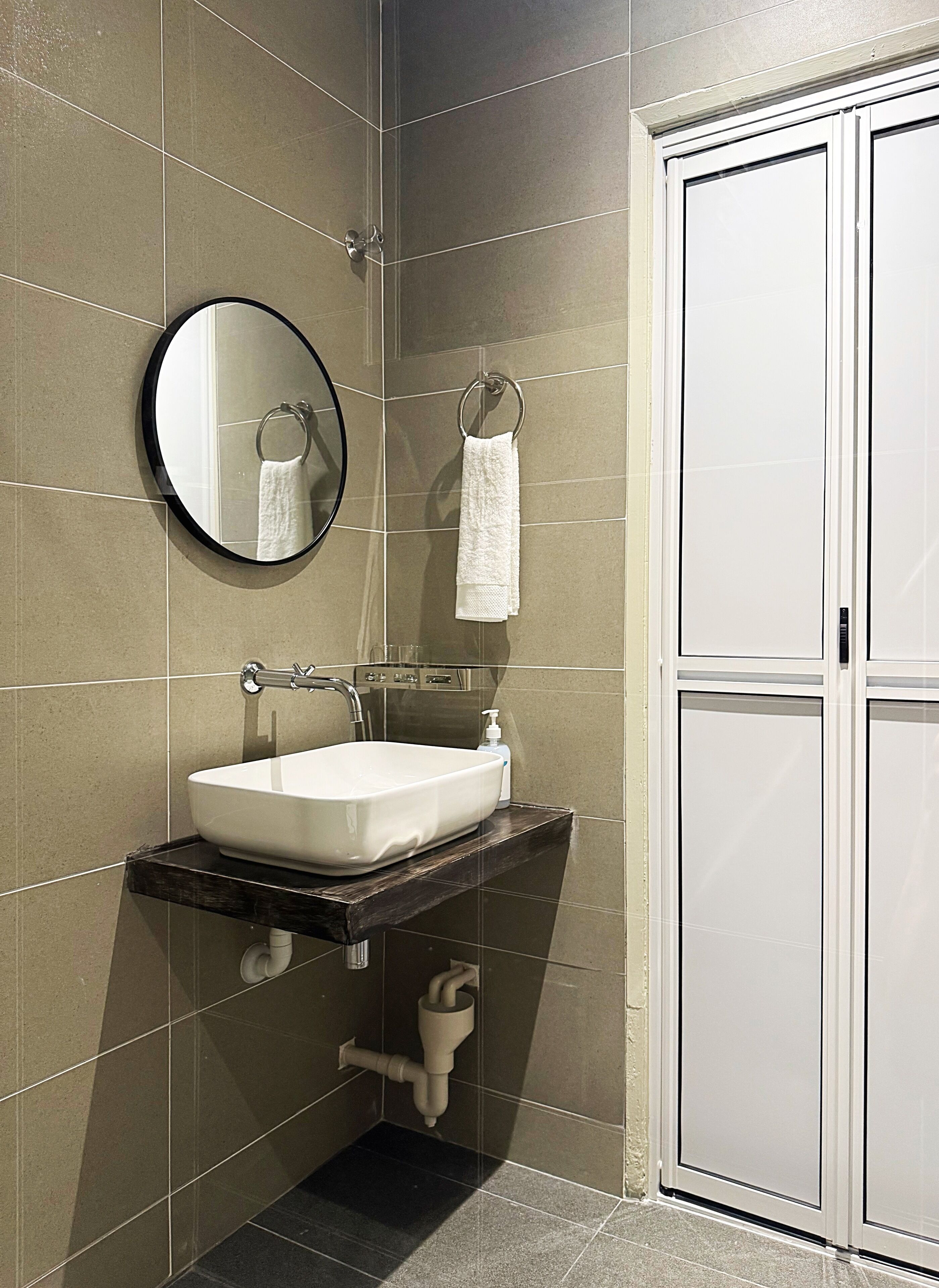 A bathroom with a white sink, a round mirror, and a towel hanging on a metal ring.
