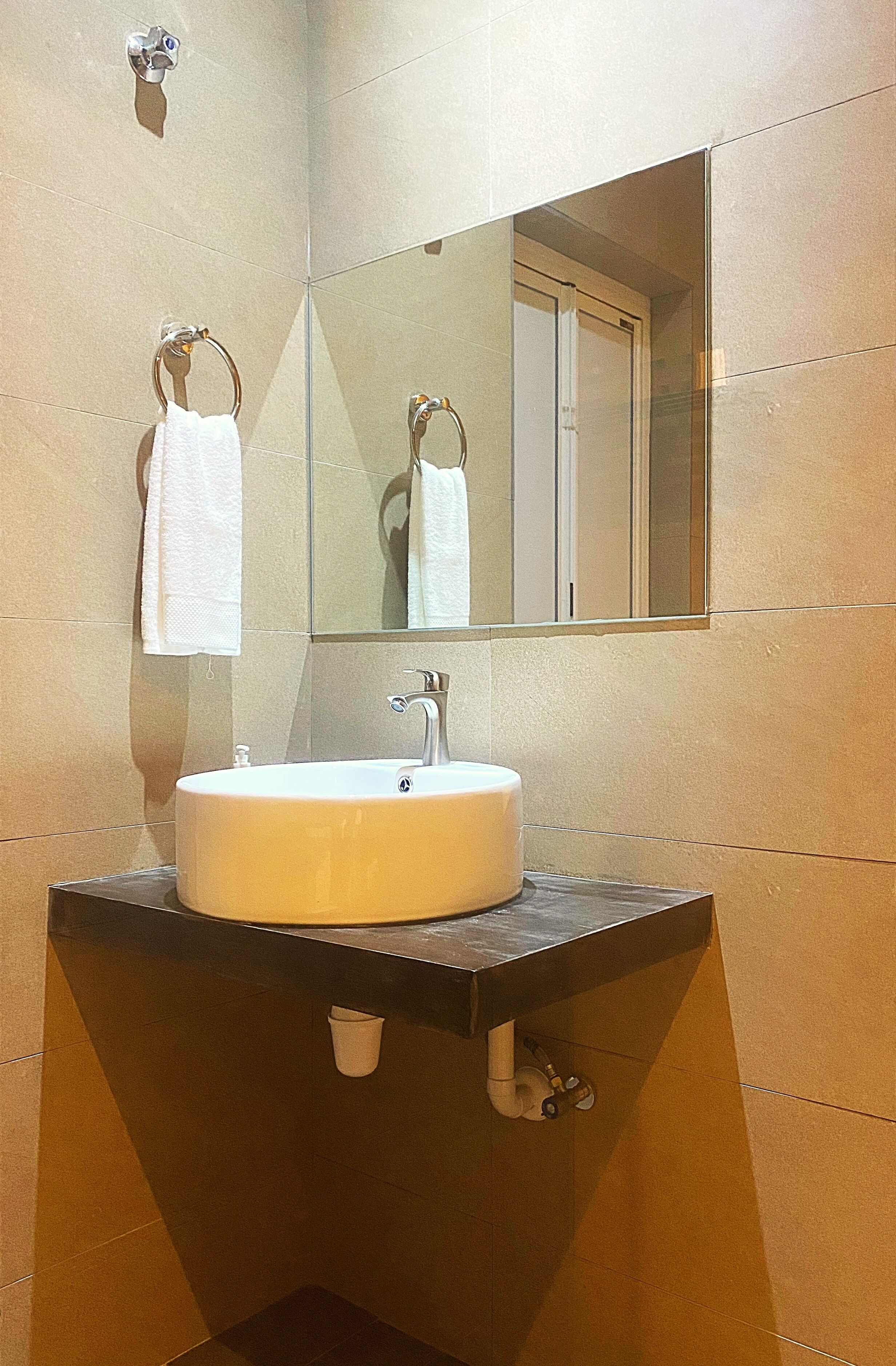 A bathroom with a round sink, a mirror, and two white towels hanging on hooks.