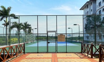 A fenced tennis court with a clear view of the surrounding area, including a building and palm trees.