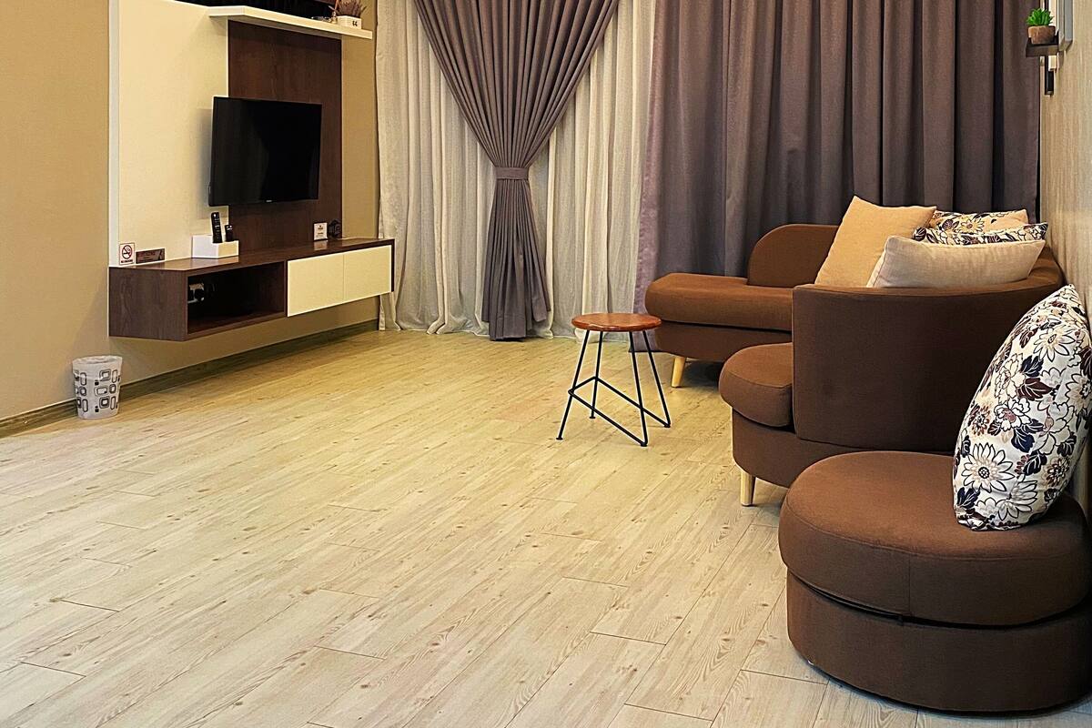 A modern living room with a flat-screen TV, a ceiling light fixture, a sofa, a small stool, and a large window with curtains.