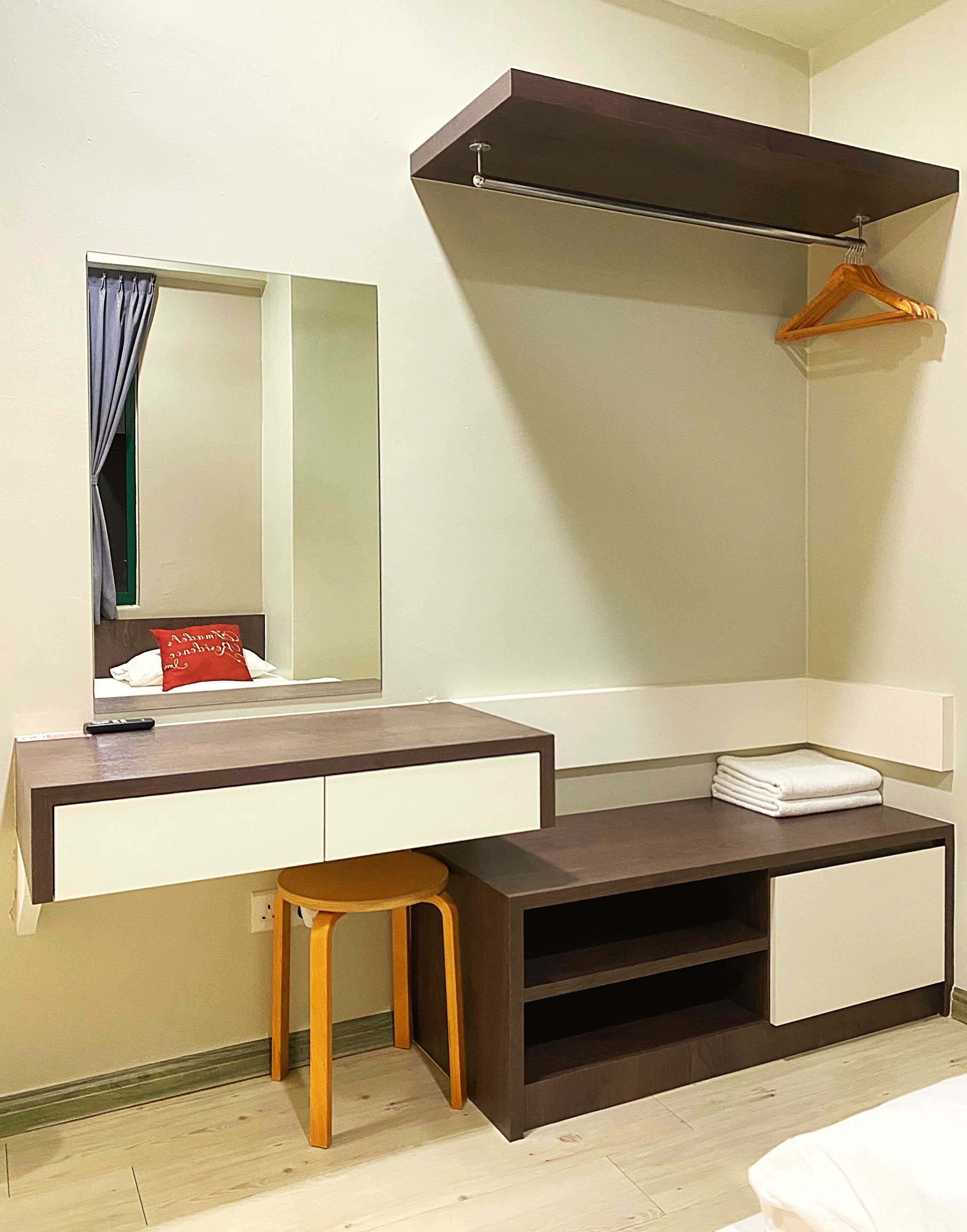 Habitación compacta con escritorio integrado, espejo, perchero y un taburete pequeño.