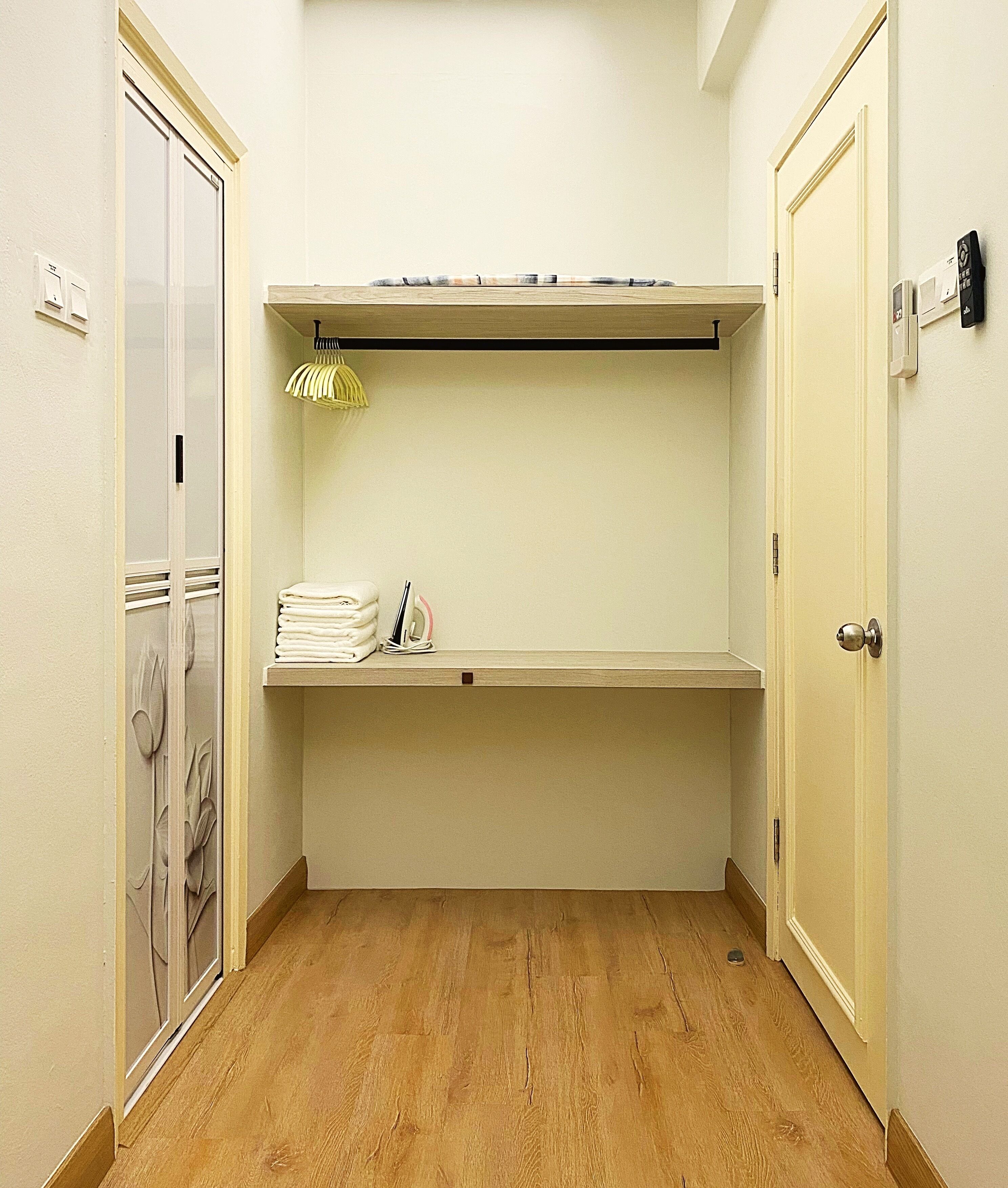 A small, narrow hallway with a wooden floor, a built-in shelf with folded towels, and a door with a lock.