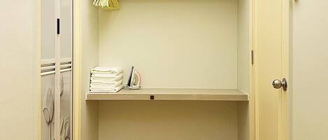 A small, narrow hallway with a wooden floor, a built-in shelf with folded towels, and a door with a lock.