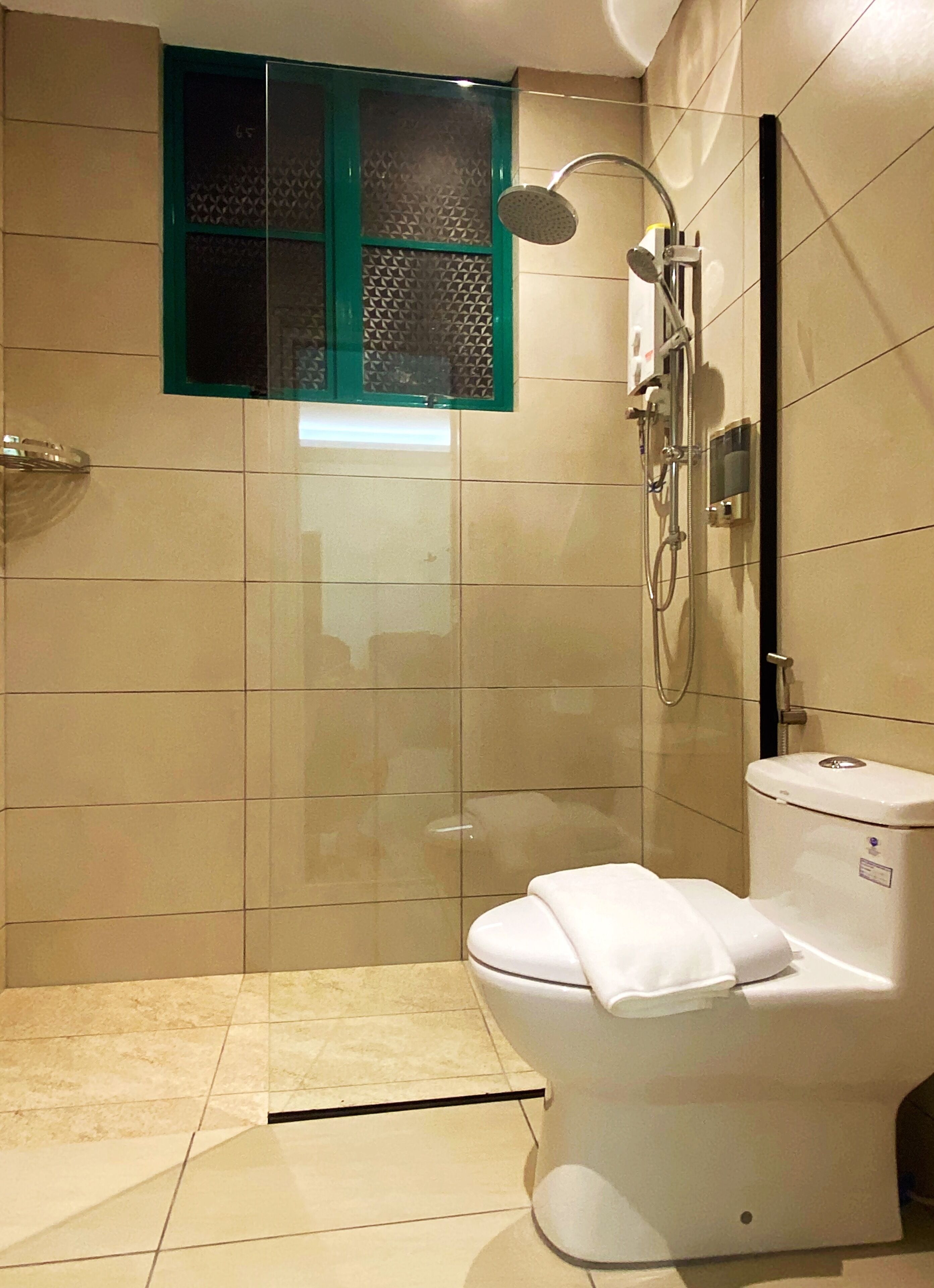 Ein modernes Badezimmer mit Dusche, Toilette und einem Fenster mit grünem Rahmen.