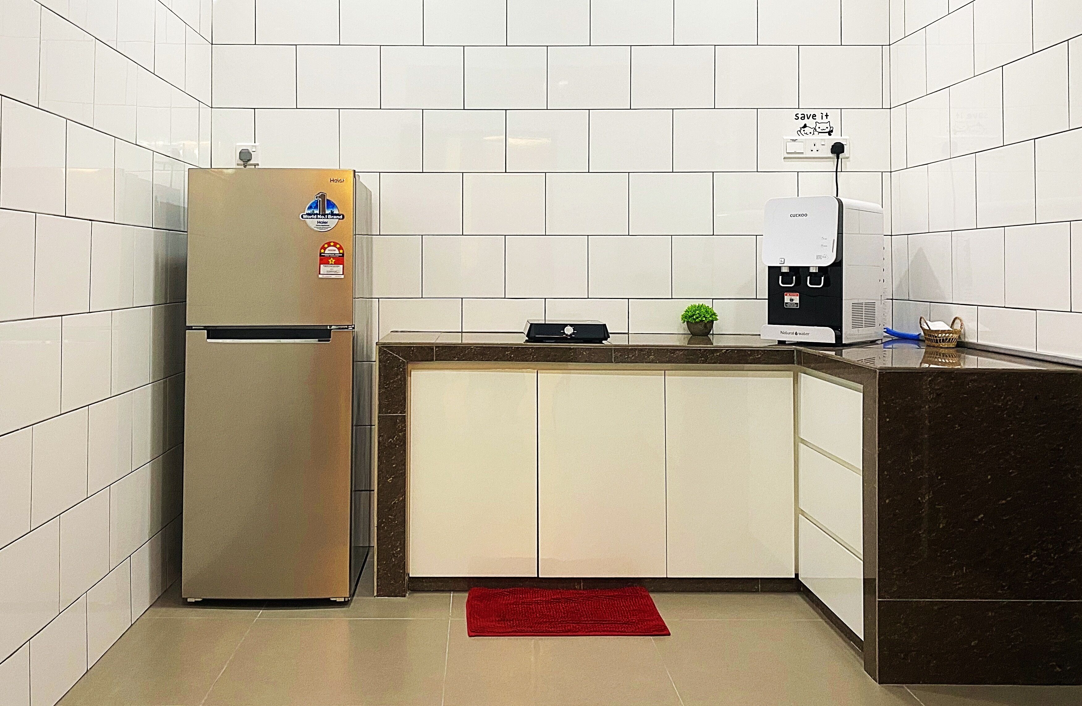 A compact kitchen with a stainless steel refrigerator, a coffee machine, and a small potted plant.