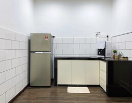 Cocina compacta con paredes de azulejos blancos, suelo de madera, refrigerador, cafetera y una pequeña planta en maceta.