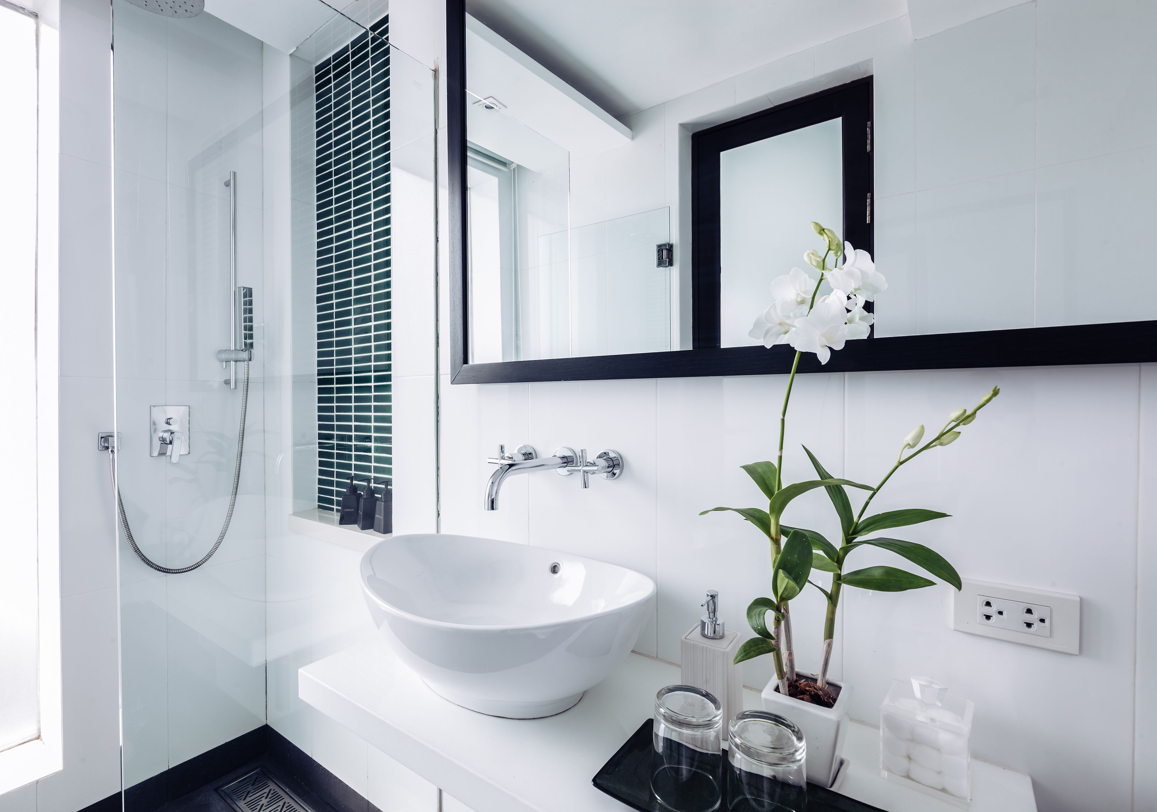 Un baño moderno con un lavamanos blanco, un espejo grande y una orquídea en maceta.