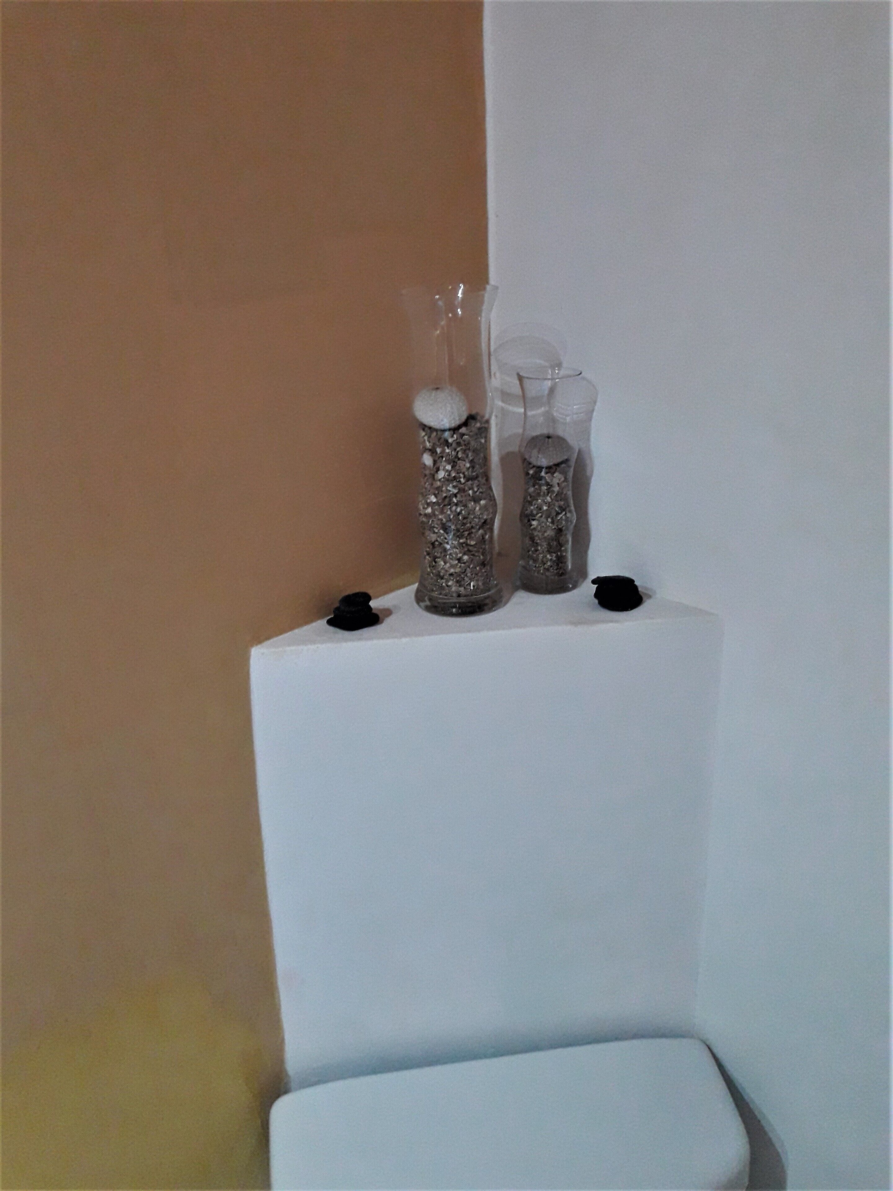 Un pedestal blanco con tres jarrones de vidrio que contienen guijarros y un objeto pequeño en la parte superior.