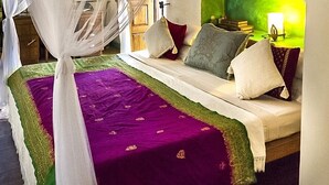 Een kamer met een bed, een groen hoofdeinde, een nachtkastje met een lamp en een raam met gordijnen.