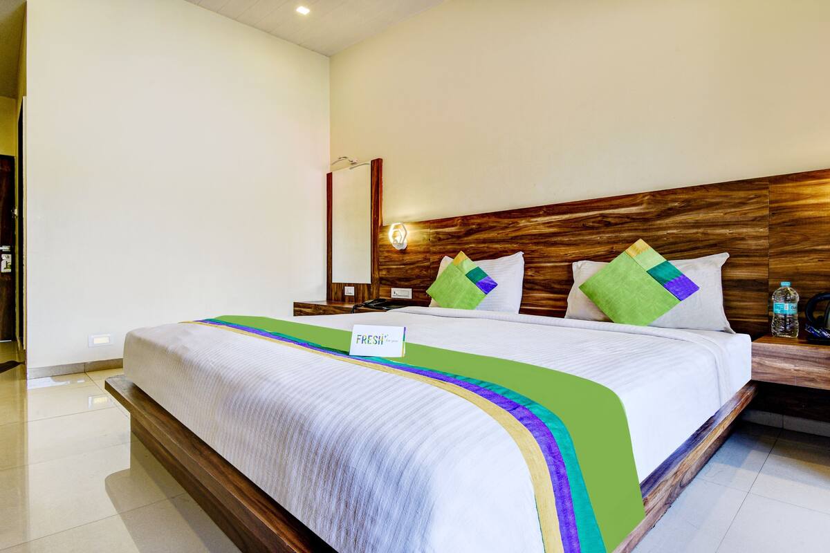 A hotel room with a large bed, wooden headboard, and a bedside table with a kettle and water bottle.