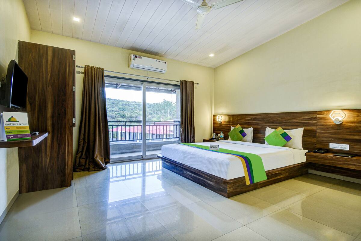 A hotel room with a bed, a television, a window with curtains, and a ceiling fan.