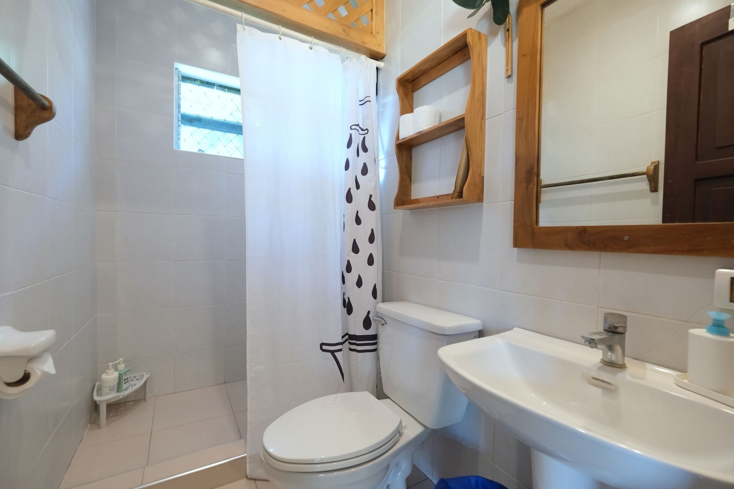 A bathroom with a toilet, shower curtain, sink, and wooden shelf.
