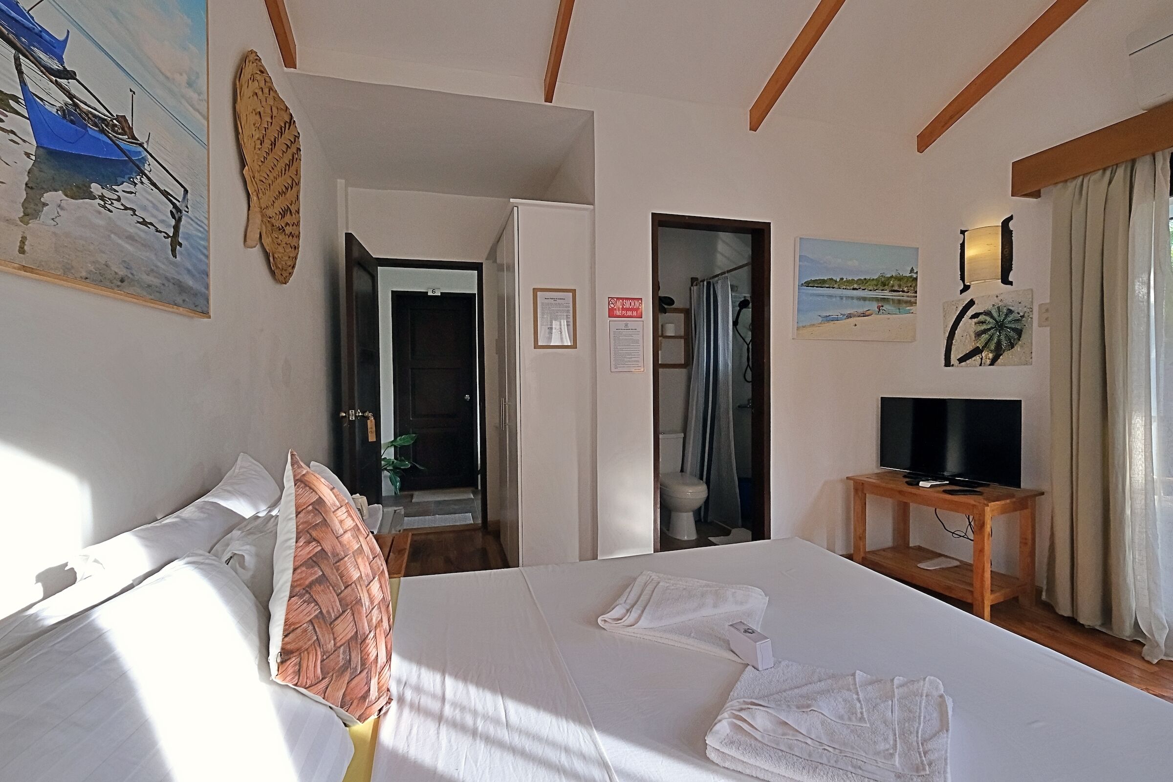 Hotelkamer met een bed, een televisie op een houten standaard, een schilderij van een boot aan de muur, en een ingelijst certificaat aan de muur.