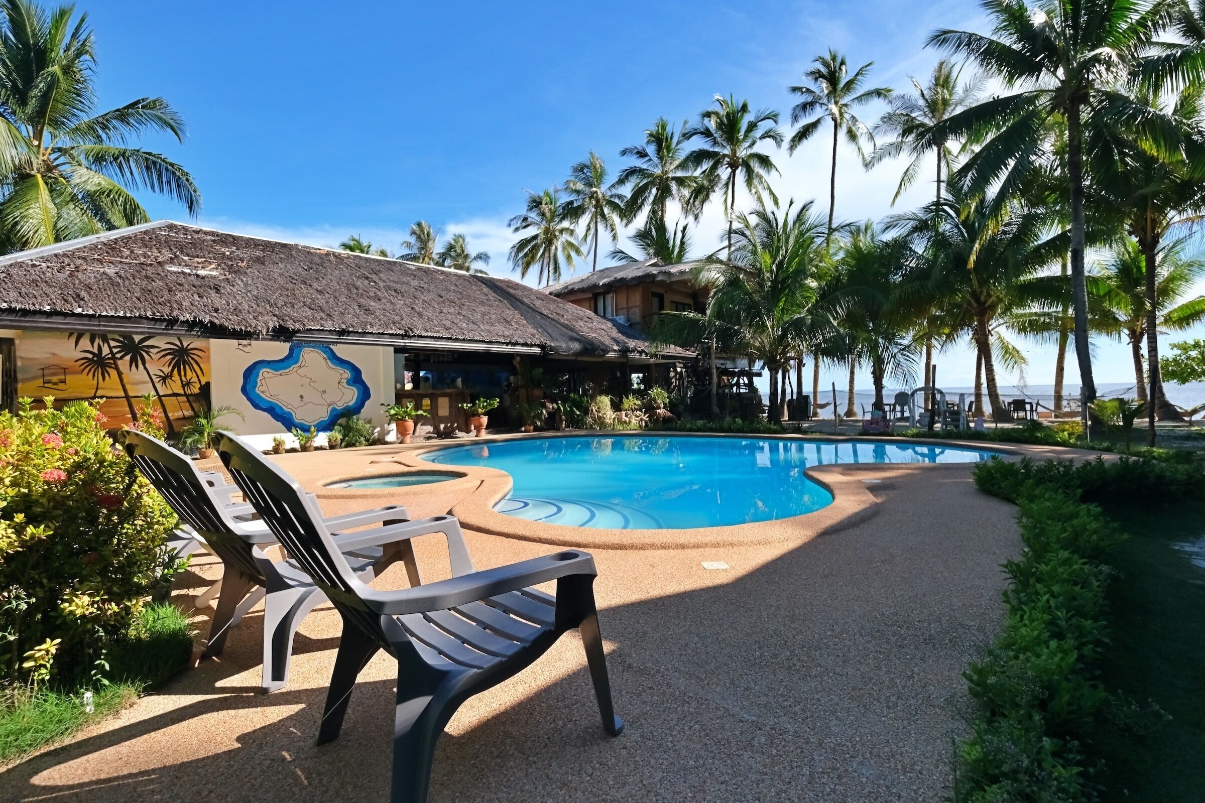 A pool area with lounge chairs, a thatched-roof building, and palm trees.
