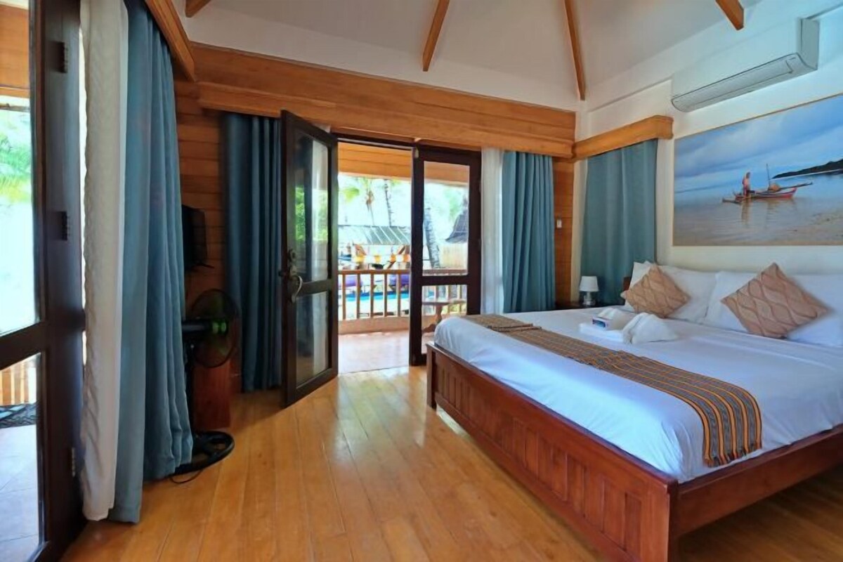Un dormitorio amplio con una cama grande, suelo de madera y vistas a la playa a través de una puerta abierta.