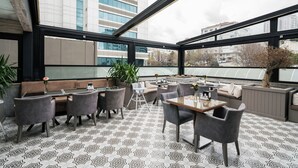 A modern outdoor seating area with tables and chairs, large windows, and potted plants. - Orya Hotel (Istanbul)