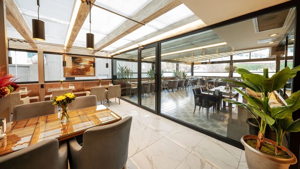 A modern dining area with glass walls, a wooden ceiling, and a view of the outdoors. - Orya Hotel (Istanbul)