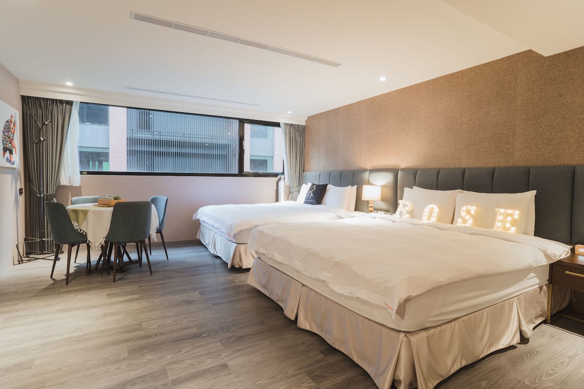 Habitación de hotel con dos camas, un comedor y un ventanal grande.